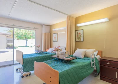 A shared patient room with two medical beds and a large sunny window