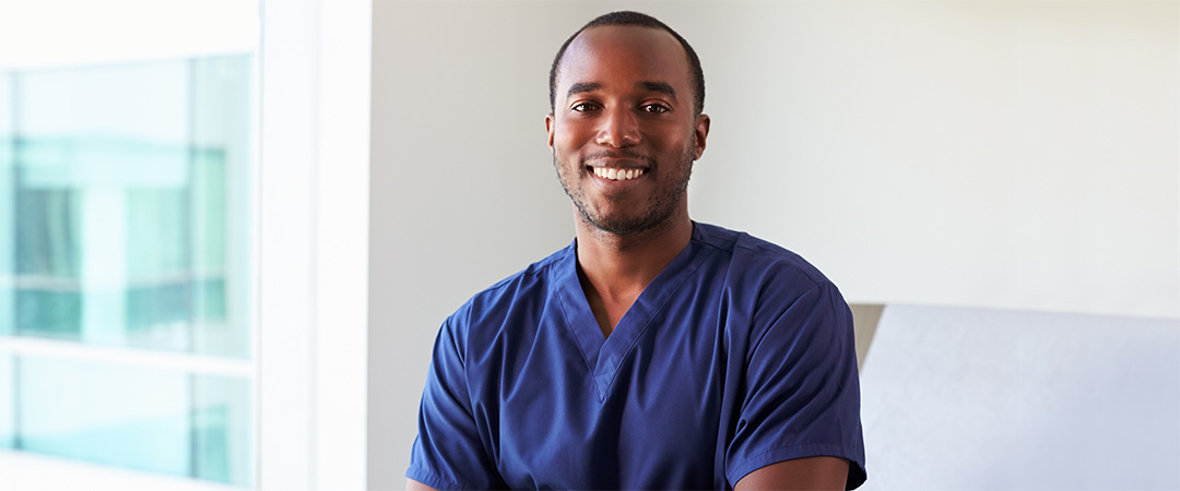 A male nurse wearing blue scrubs smiling