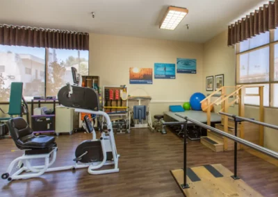 Indoor recreation area with a small stage, stationary bike, and balance platform for physical therapy sessions at the Meadows on Sunset facility
