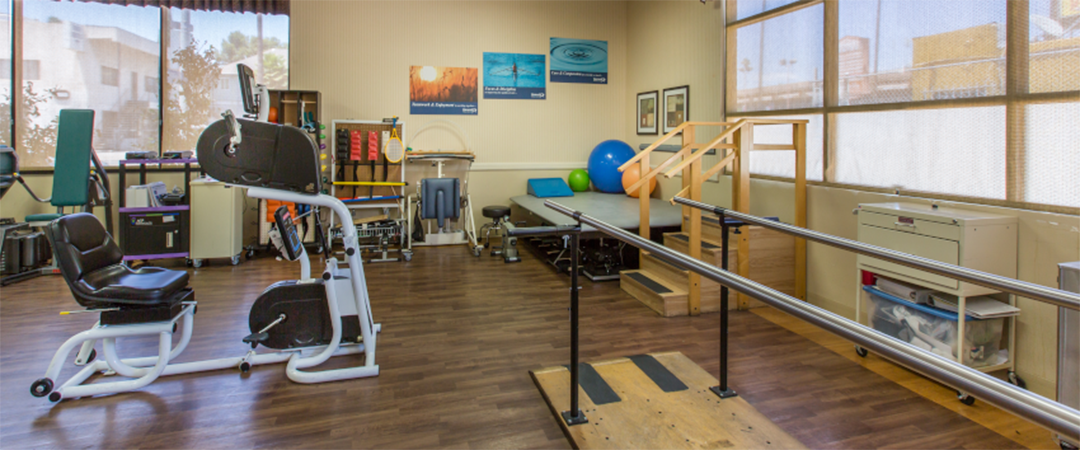 Indoor recreation area with a small stage, stationary bike, and balance platform for physical therapy sessions at the Meadows on Sunset facility